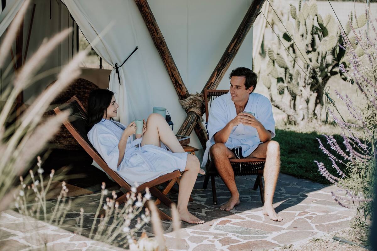 Two people sitting on lounge chairs outside a building, with a rope and wooden structure in the background.