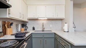 A compact kitchen with white cabinets, a built-in stove, and a marble countertop. - Gros Ventre B7: Newly remodeled, pristine condo in Teton Village (Teton Village)