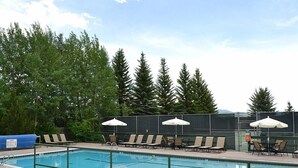 A swimming pool with lounge chairs and umbrellas, surrounded by trees. - Gros Ventre B7: Newly remodeled, pristine condo in Teton Village (Teton Village)