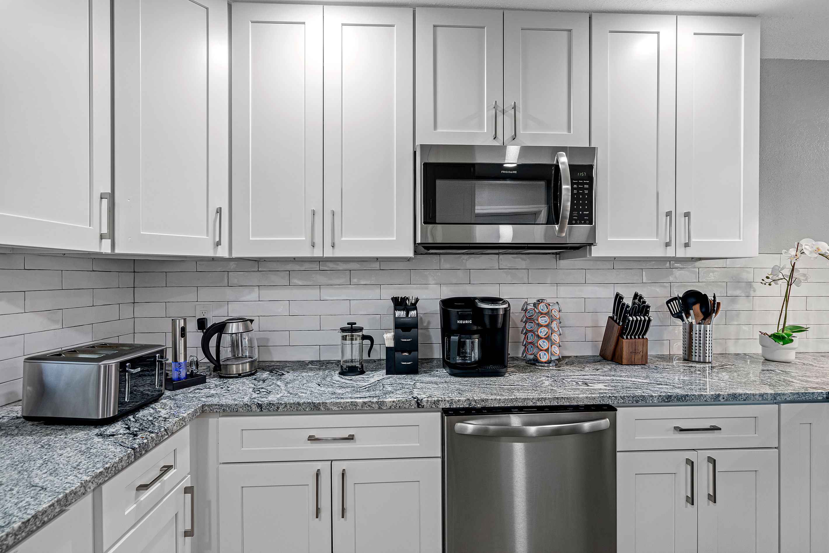 A modern kitchen with white cabinets, a stainless steel microwave, a coffee maker, and a toaster.