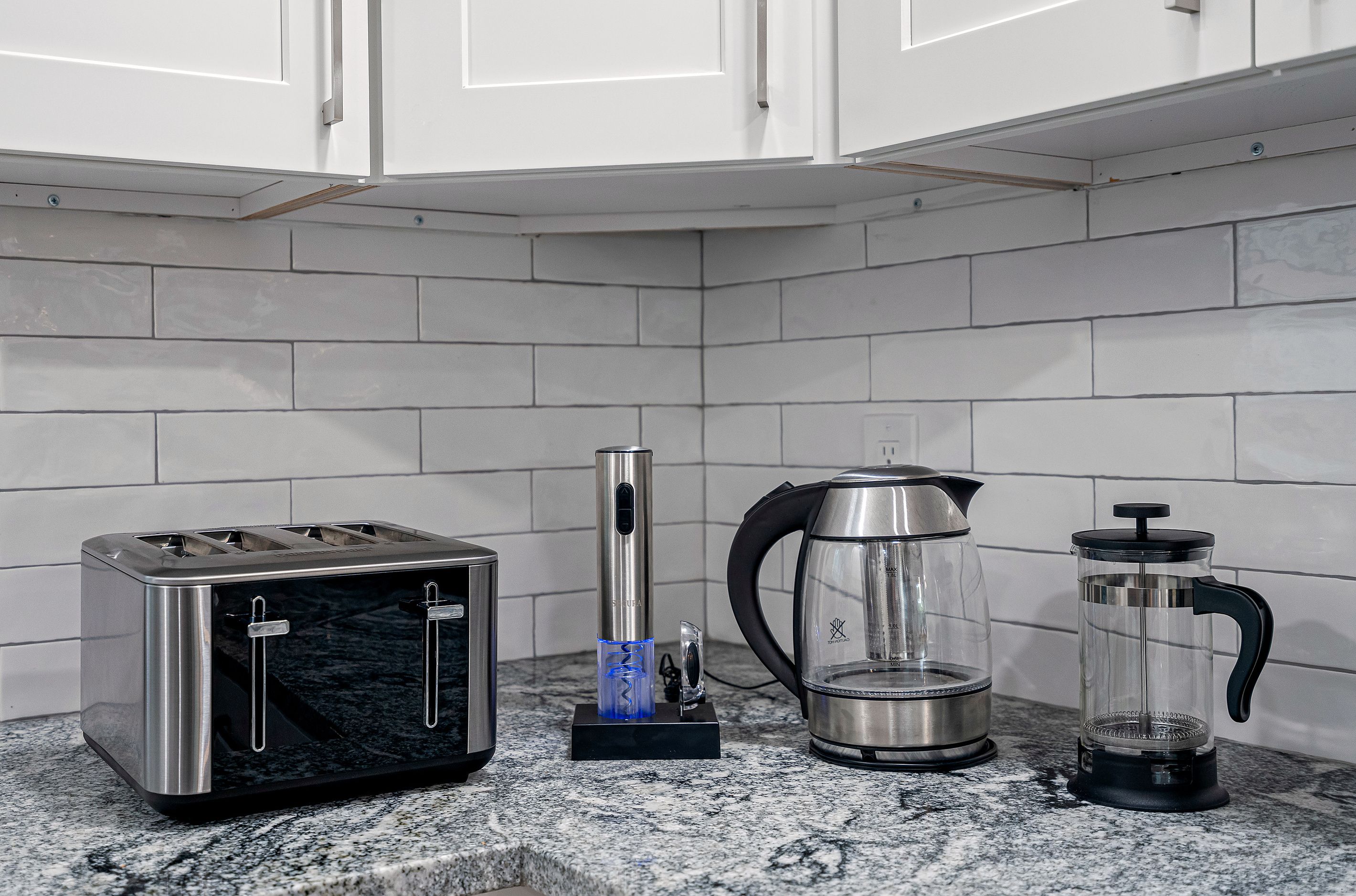 A kitchen with a toaster, a coffee maker, and a French press on a granite countertop.