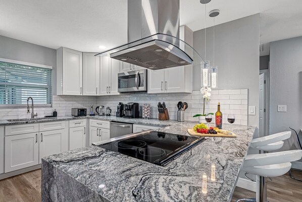 A modern kitchen with white cabinets, a built-in microwave, a stainless steel range hood, and a granite countertop.