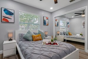 Ein modernes Schlafzimmer mit einem großen Bett, einem Nachttisch, einem Beistelltisch, einem Spiegel und Kunstwerken an den Wänden.