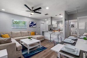 Ein modernes Wohnzimmer mit einer Couch, einem Couchtisch und einem Essbereich mit Stühlen und einem für eine Mahlzeit gedeckten Tisch.