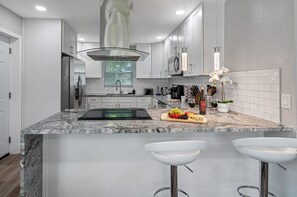 A modern kitchen with white cabinets, a granite countertop, a built-in oven, and a stainless steel refrigerator.