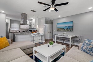 A modern living room with a white sofa, a coffee table, and a dining area with a white table and chairs.