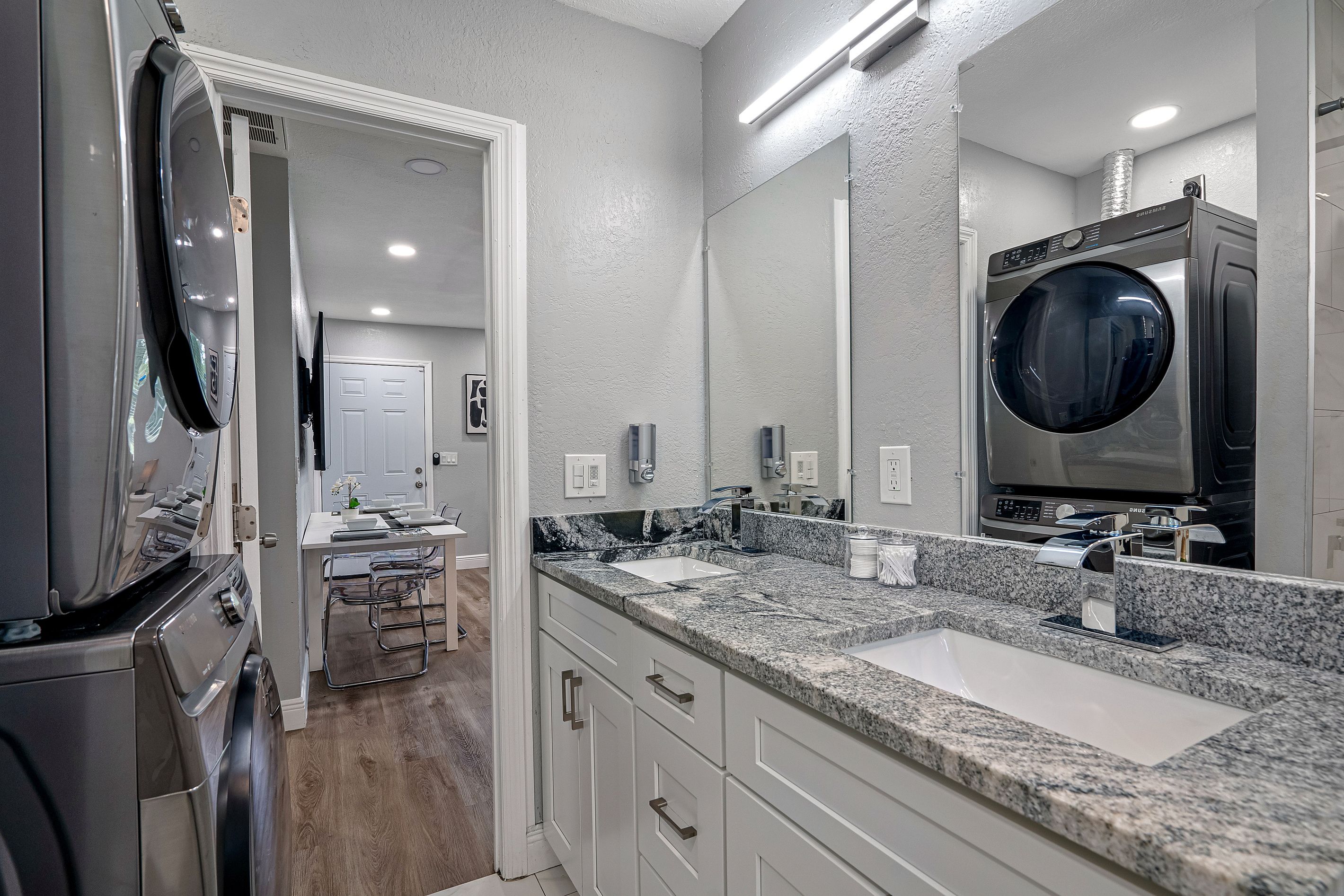 A modern bathroom with a large mirror, a built-in washing machine, and a countertop with a sink.