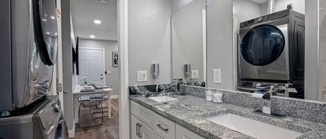A modern bathroom with a large mirror, a built-in washing machine, and a countertop with a sink.
