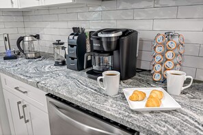 A kitchen with a coffee maker, a kettle, a coffee pot, and a plate with croissants.