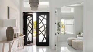 Un intérieur moderne avec une porte à cadre noir, un lustre, un canapé blanc et une petite table avec une lampe.