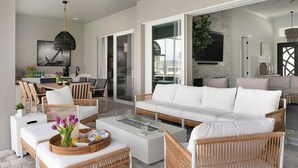 Un salon moderne avec un canapé blanc, des fauteuils en osier, une table basse en verre et un coin repas comprenant une table et des chaises.