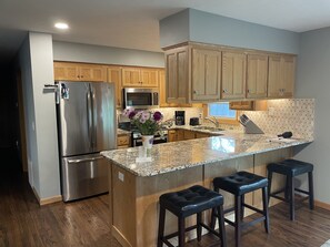 A modern kitchen with wooden cabinets, stainless steel appliances, a granite countertop, and bar stools. - NEW- Wayne's Place! WEST OMAHA, COMPLETE REMODEL, Quality Comfort (Omaha)