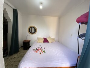 A small, clean room with a bed, a round mirror, a small table, and a bunk bed.