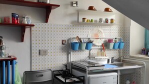 A compact kitchen with a radiator, a sink, and a coffee machine. There are shelves with kitchenware and a window with blinds. - Small nest toino (Torino)