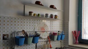 A kitchen with white tiles, shelves with dishes, and utensils hanging on a rack. - Small nest toino (Torino)