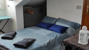 A bedroom with a bed, two pillows, a blanket, a small table, and a hanging rack. - Small nest toino (Torino)