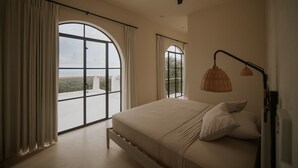 Een slaapkamer met een groot bed, twee ramen en een plafondventilator.