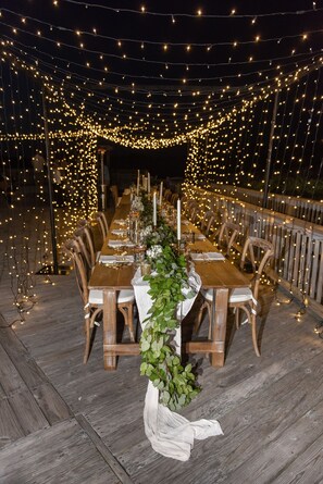 Enjoy meals al fresco in a charming outdoor dining area with a long table, surrounded by comfortable seating and warm ambiance.