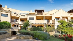 A multi-story residential building with balconies, a courtyard, and a garden with red flowers. - Apartment in Las Mimosas de Banús for 4 people | 22E (Puerto Banús - Marbella)