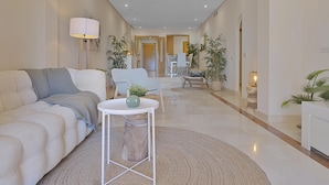 A modern living room with a sofa, a small round table, and a dining area in the background. - Apartment in Las Mimosas de Banús for 4 people | 22E (Puerto Banús - Marbella)