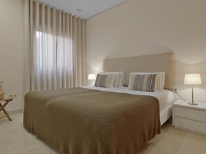 A neatly arranged hotel room with a large bed, two bedside tables, a lamp, and a window with curtains.