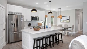 A modern kitchen with white cabinetry, stainless steel appliances, and black bar stools. - 2-Minute walk to the beach! Dog & Kid Friendly! (Crystal Beach)