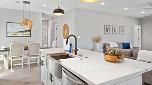 A modern kitchen with a central island, pendant lighting, and a dining area with chairs and a table. - 2-Minute walk to the beach! Dog & Kid Friendly! (Crystal Beach)