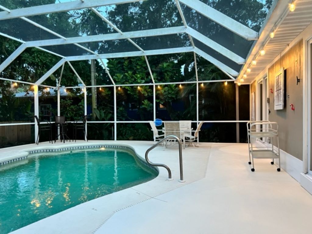 A covered outdoor swimming pool with a glass roof, surrounded by chairs and tables, and a wooden deck area.