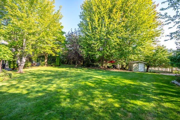 A well-maintained backyard with a lawn, a small shed, and a red umbrella. - Munson Mountain Estates (Penticton)