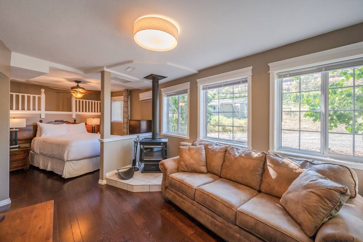 A cozy room with a bed, a sofa, a fireplace, and large windows.