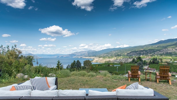 A scenic outdoor seating area with a view of a lake and mountains. - Munson Mountain Estates (Penticton)