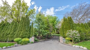 A gated driveway leading to a property with a well-maintained lawn and various trees. - Munson Mountain Estates (Penticton)
