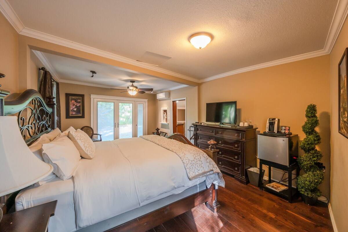 A bedroom with a large bed, a ceiling fan, a TV, and a dresser.