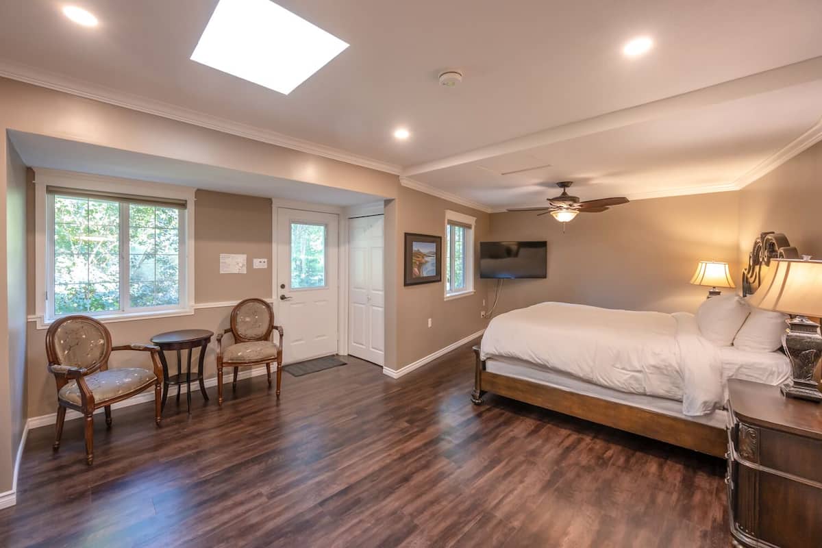 A bedroom with a large bed, a ceiling fan, a TV, and two chairs.