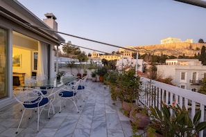 A terrace with a glass table and chairs, potted plants, and a view of ancient ruins.