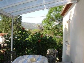 A covered patio with a table and chairs, surrounded by lush greenery and a view of distant hills. - Apartment near the beach (100 meters). (ARGELES SUR MER)
