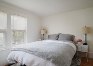 Ein Schlafzimmer mit einem Bett, zwei Nachttischen, einem Fenster und einem Beistelltisch mit einer Lampe.