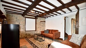 A cozy living room with a stone wall, wooden beams, a black refrigerator, a brown sofa, a patterned rug, and a white chair. - Charming holiday home - 10 min from Durbuy (Durbuy)