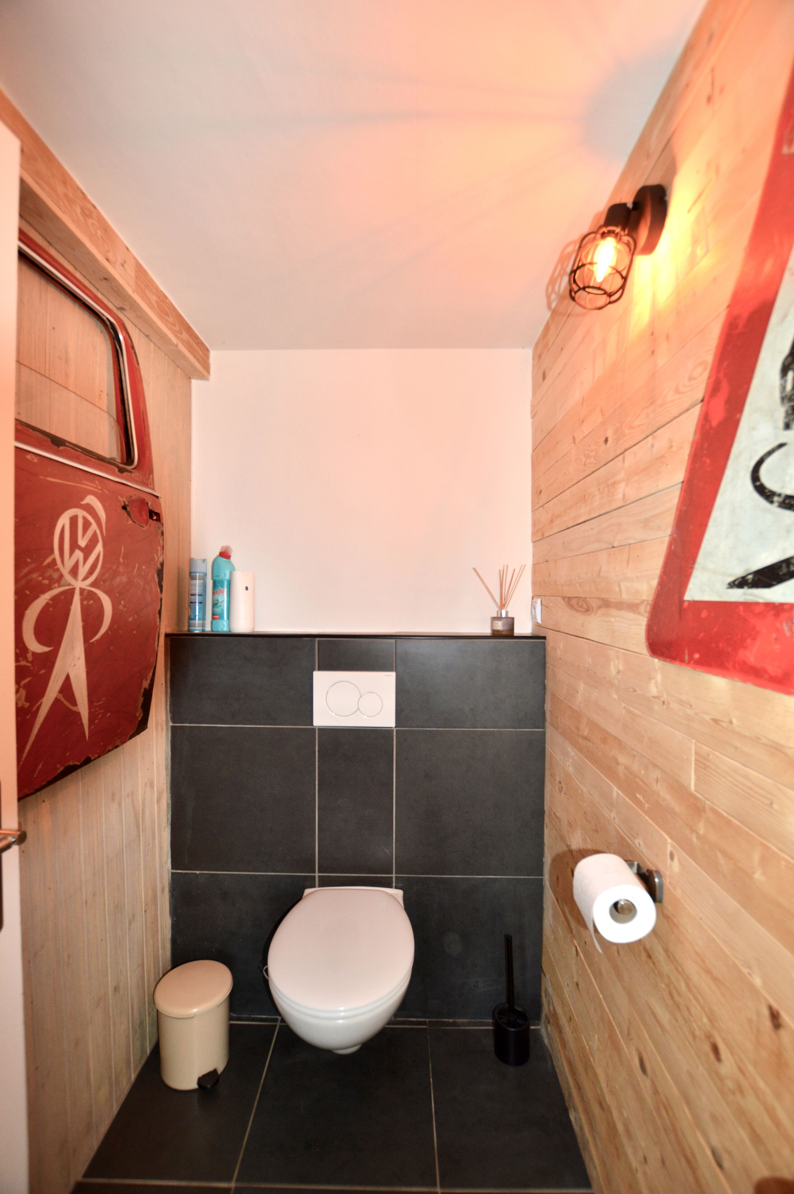 Ein kleines Badezimmer mit Toilette, Mülleimer und Toilettenpapierhalter an der Wand.