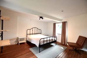 Une chambre avec un lit simple, une chaise, une petite table et une fenêtre avec des rideaux.