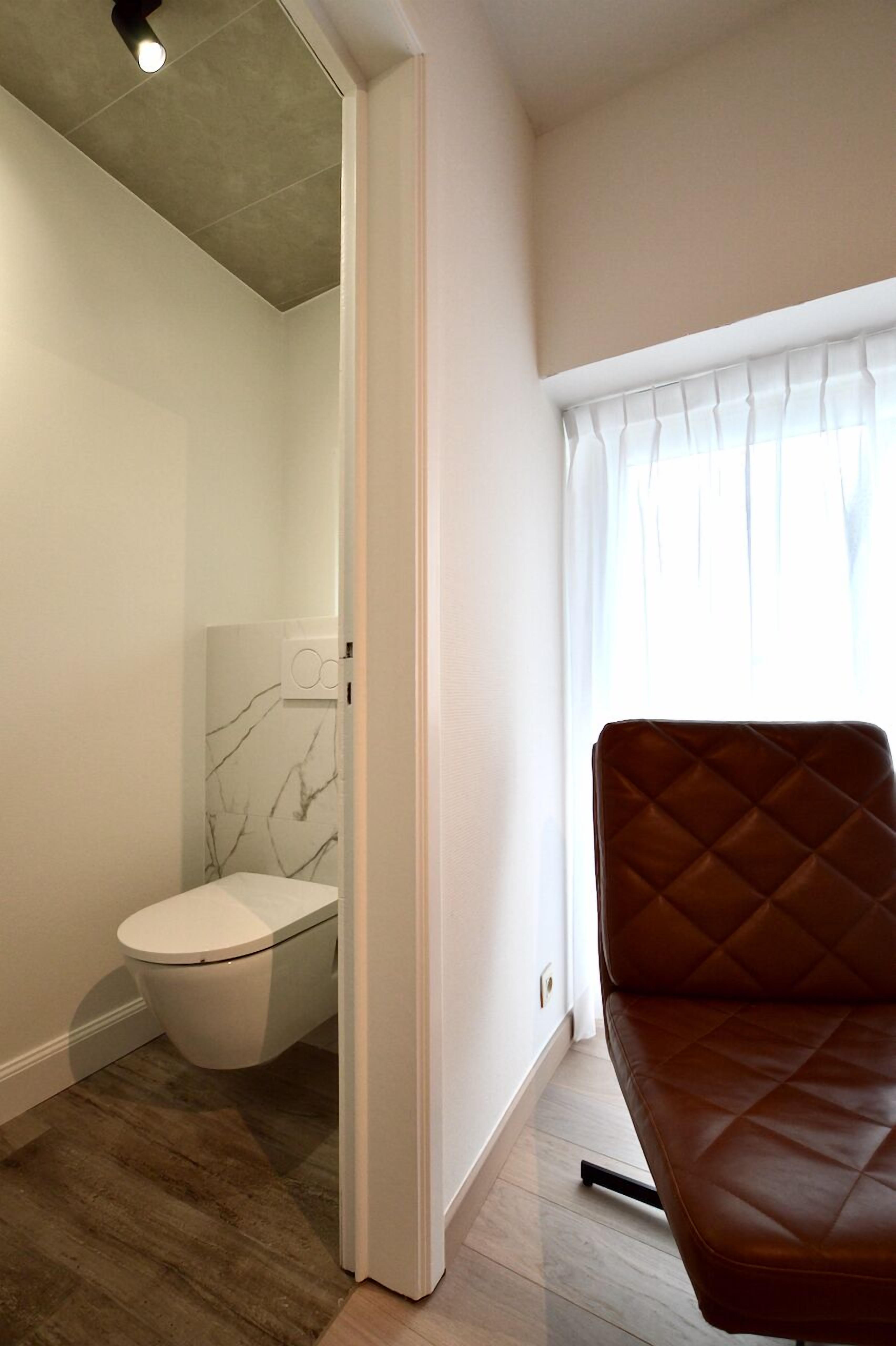 A modern bathroom with a toilet, a marble wall, and a brown leather chair.