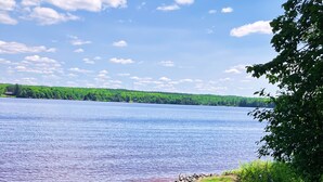 A lakeside view with a row of blue Adirondack chairs and a wooden bench on a grassy area. - Cabin right on the water! All bikers, skiers, fisherman, and more welcome! (Cable)