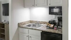 Una cocina funcional con armarios blancos, encimera de granito, pileta de acero inoxidable, cafetera y lavavajillas.