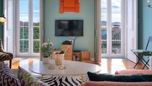 A living room with a round table, a flat-screen TV, and a large window.