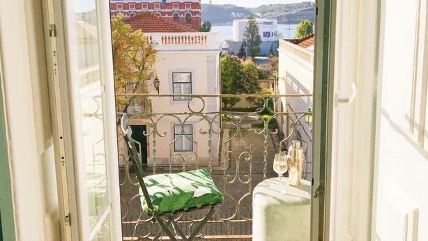 A balcony with a view of a building with red-tiled roofs, a white building with a window, and a body of water in the background.