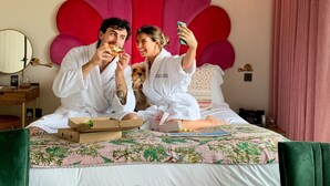 Una habitació amb un llit gran, una taula rodona amb dues begudes i un gos.