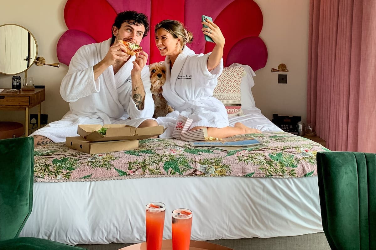 Una habitación con una cama grande, una mesa redonda con dos bebidas y un perro.
