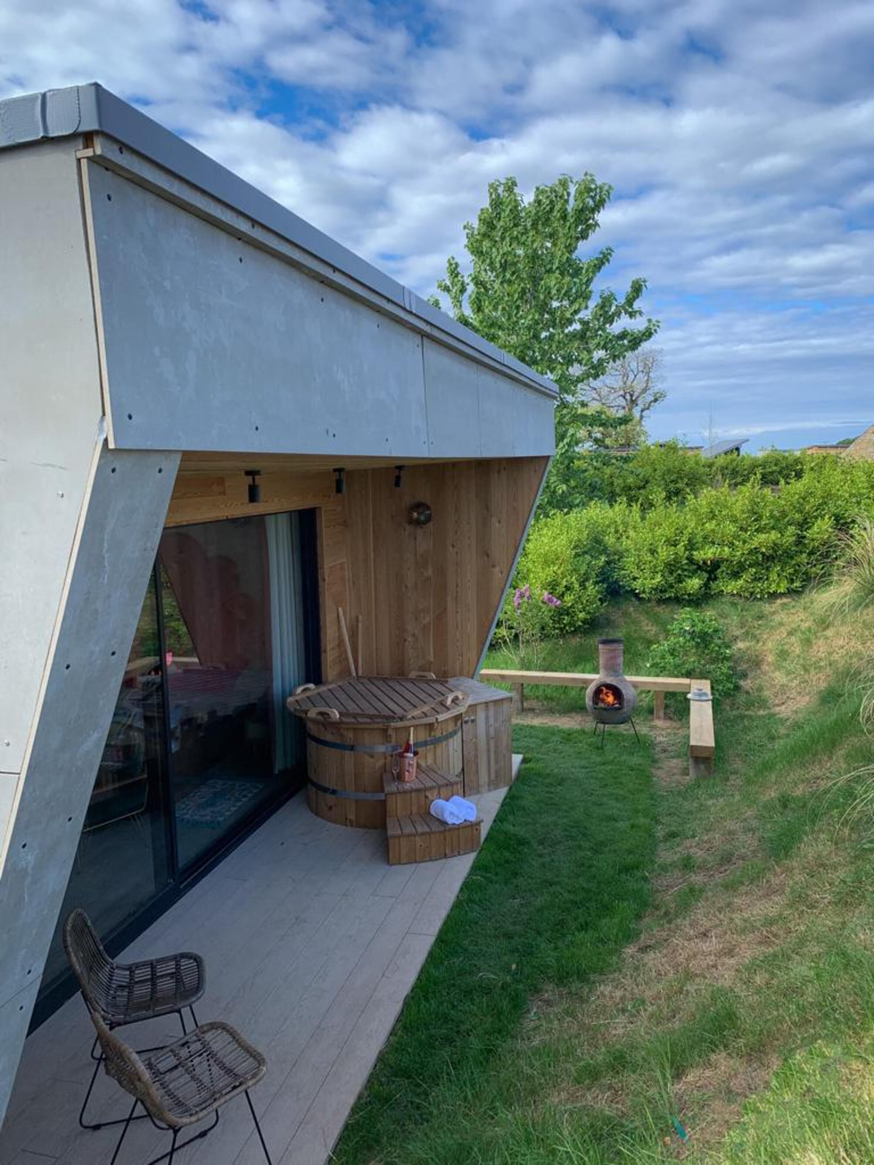 A modern house with a large glass door, a wooden deck, a hot tub, and a wood-burning stove.
