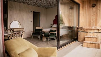 A cozy room with a wooden ceiling, a glass door leading outside, a bed with green pillows, and a wooden sauna.