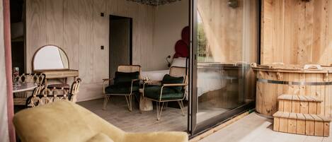 A cozy room with a wooden ceiling, a glass door leading outside, a bed with green pillows, and a wooden sauna.